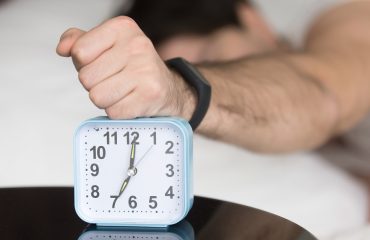 Angry sleepy young guy turning off noisy annoying alarm clock
